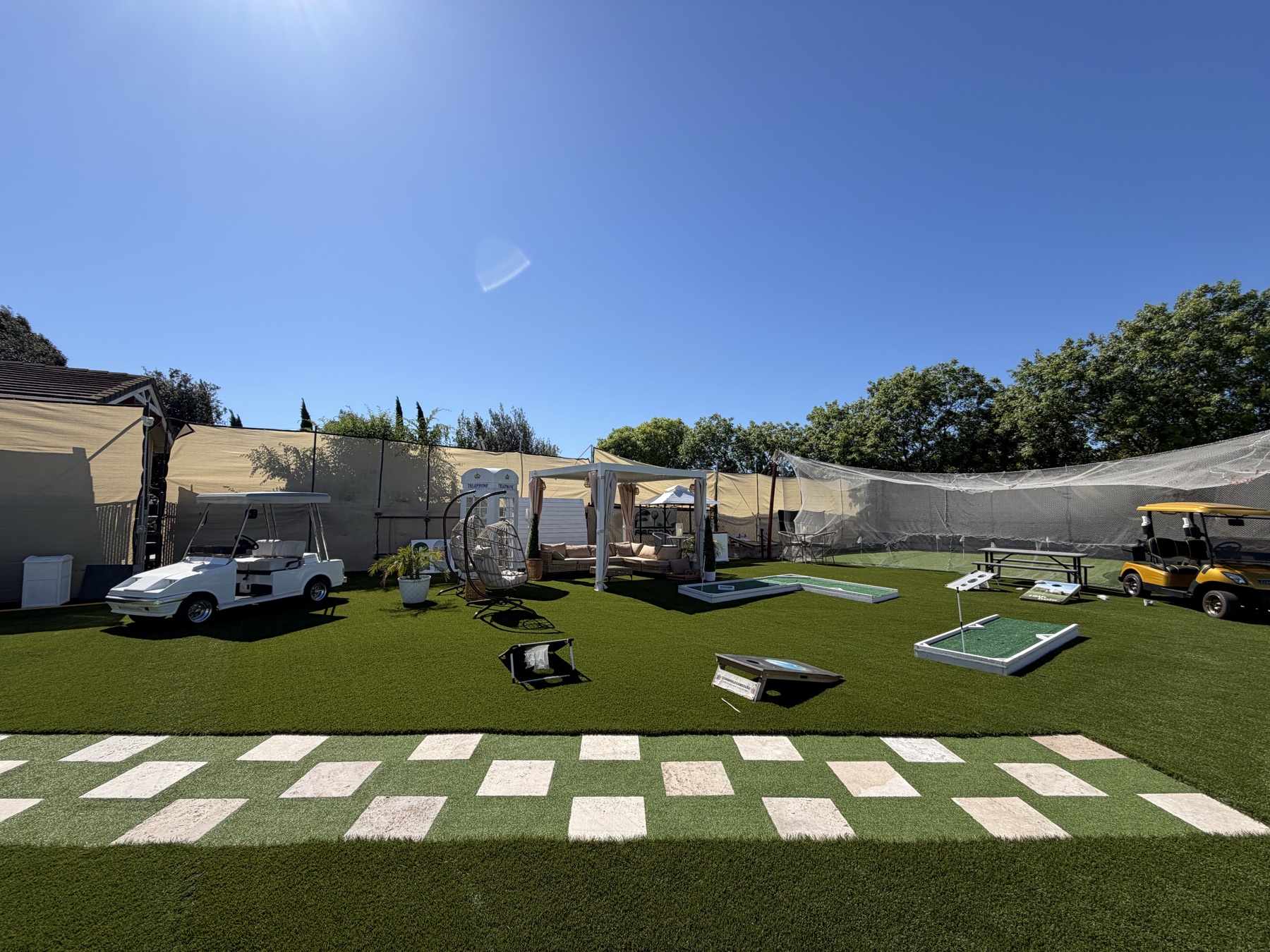 Turf backyard lounge with a shaded cabana, hanging chairs, cornhole boards and golf carts
