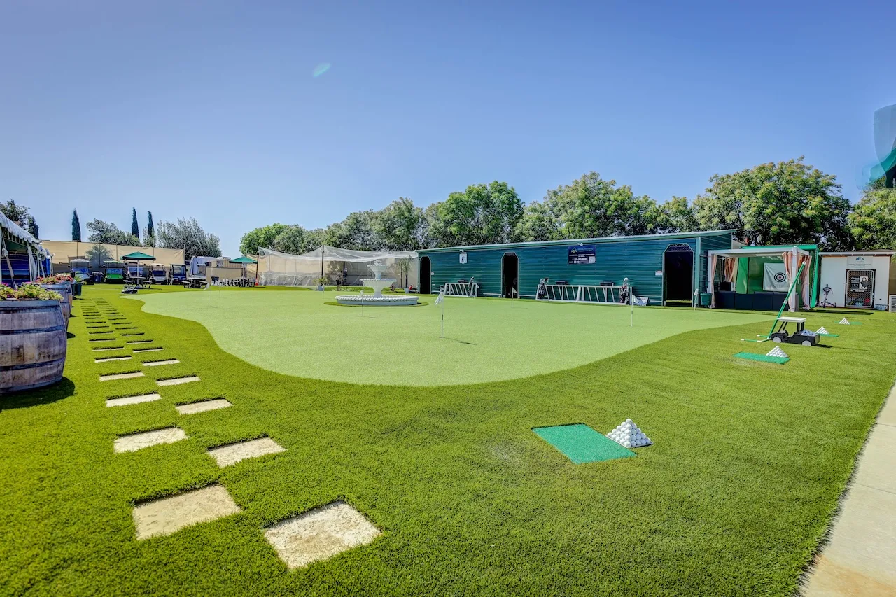 Wide view of the FixFactory practice grounds — a large putting green, hitting nets, target mats and covered bays